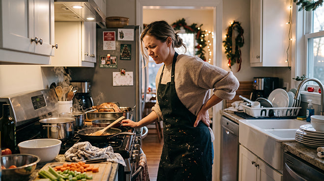 woman in kitchen cooking a holiday dinner while holding her lower back